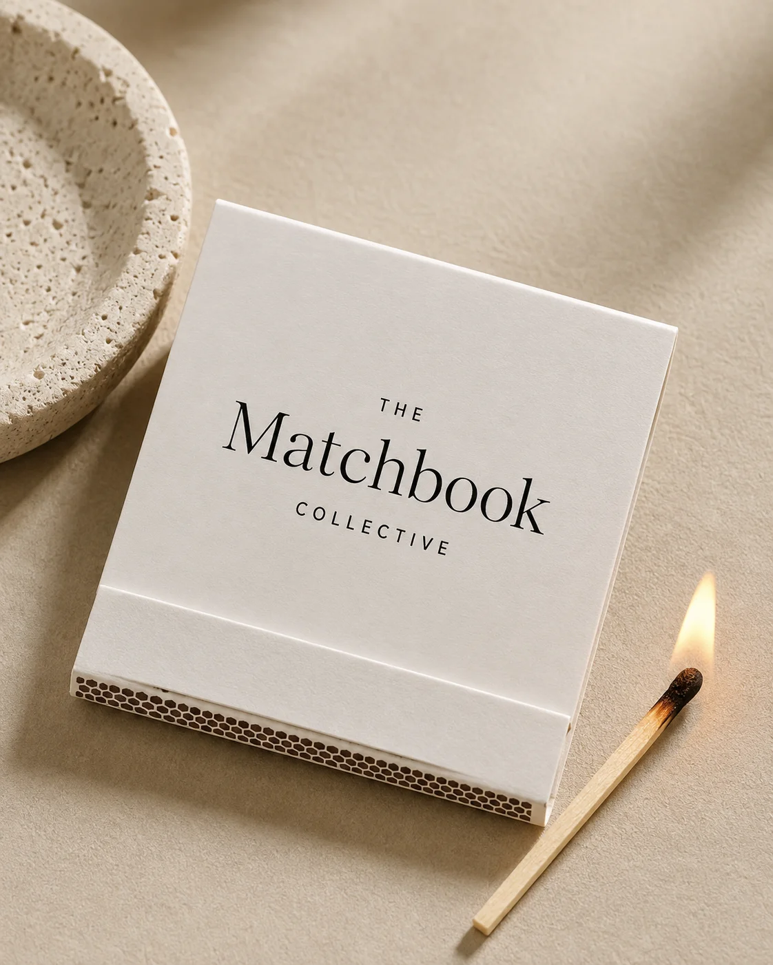 A Matchbook Collective matchbook on a warm textured surface beside a stone dish and lit match.